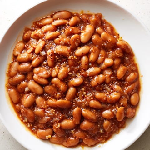 Golden brown Baked Beans simmering in a rich, savory tomato sauce for a BBQ side.
