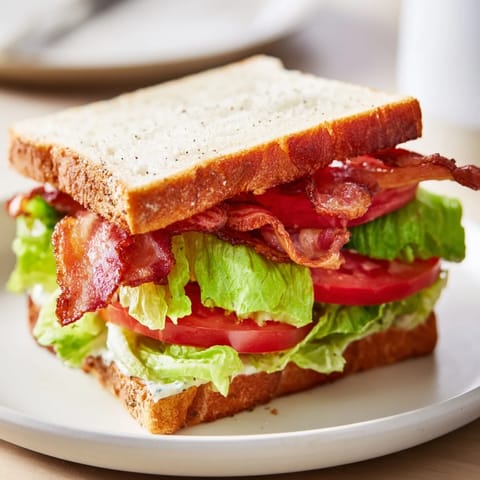 A perfectly stacked BLT sandwich shows off layers of bacon, tomato, lettuce; ready to be eaten.