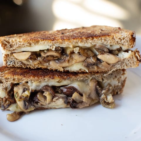 Sliced Mushroom Swiss Grilled Cheese sandwich on a rustic plate, perfect with a bowl of warm tomato soup.  