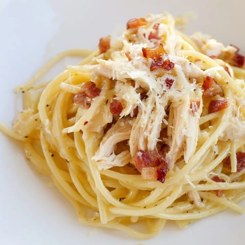 Steam rises from a bowl of Chicken Carbonara, showcasing tangled pasta, savory shredded chicken, and golden bacon, perfect for a comforting weeknight dinner.