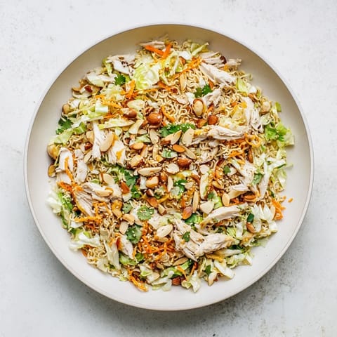 Freshly tossed crunchy ramen chicken salad served in a white bowl, topped with toasted almonds and sesame seeds.