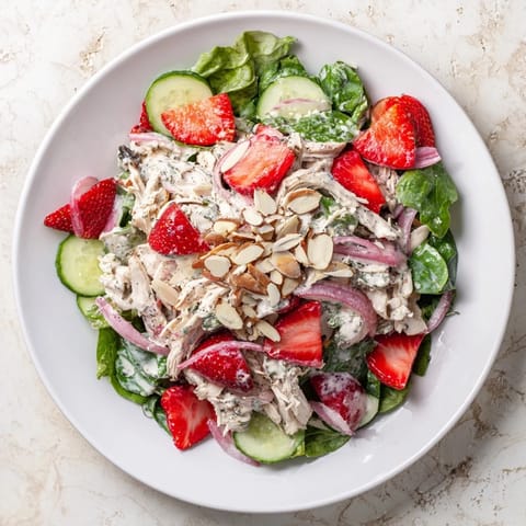 A close-up view of Strawberry Poppy Seed Chicken Salad topped with crumbled feta and toasted almonds on mixed greens.