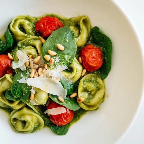 A vibrant bowl of Pesto Tortellini Salad with tender pasta, bright cherry tomatoes, and fresh spinach leaves.