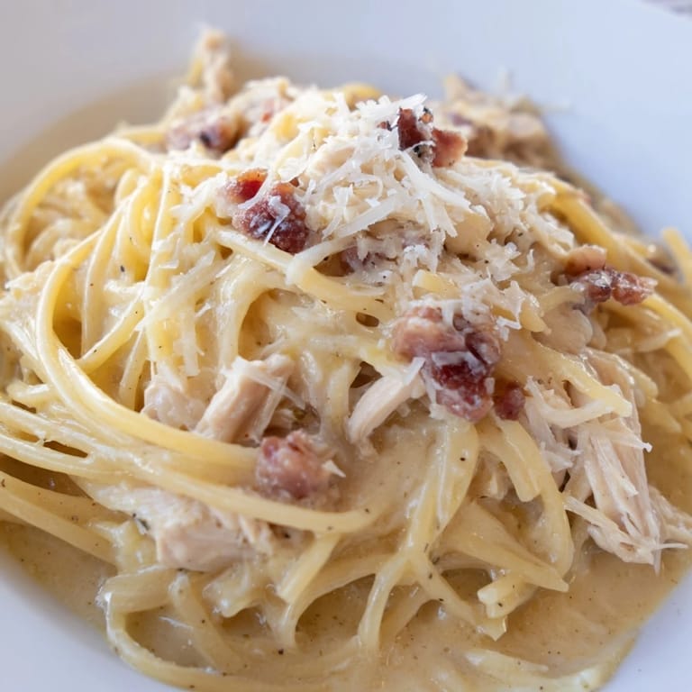 Close-up of Chicken Carbonara with glossy sauce, fresh parsley garnish, and extra grated Parmesan, served on a rustic wooden table for family-style dining.