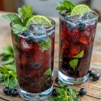 Chilled highball glasses filled with Tangy Blackcurrant Mojito, garnished with fresh mint sprigs and lime slices.